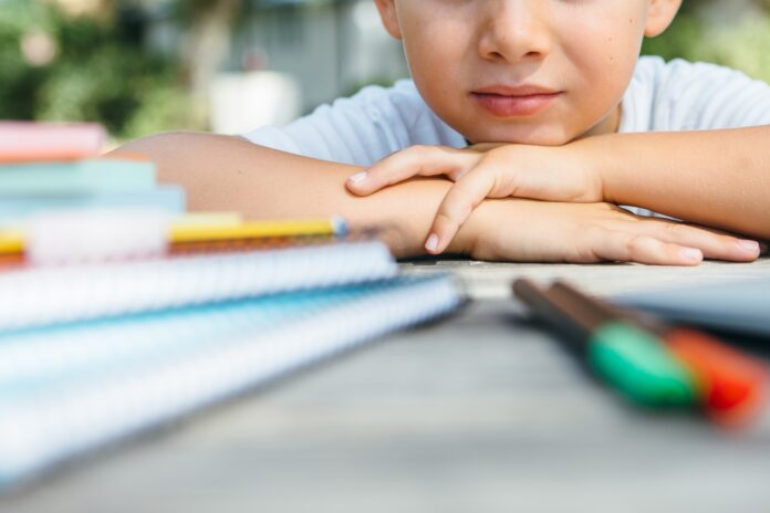 Crop child at table with school supplies