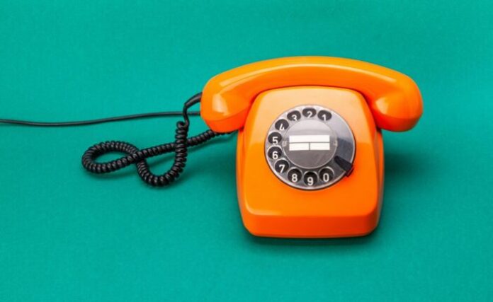 Retro phone orange color, vintage handset receiver on green background.