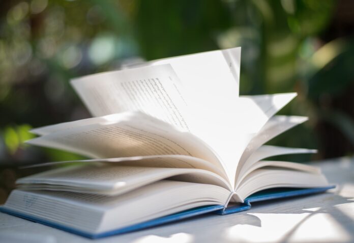 Close up of open book at home garden with nature bokeh background.