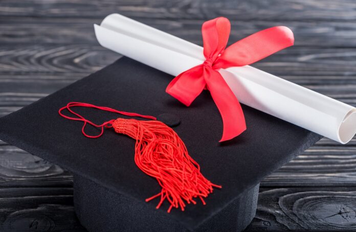 Graduation hat and diploma with red ribbon on wooden table