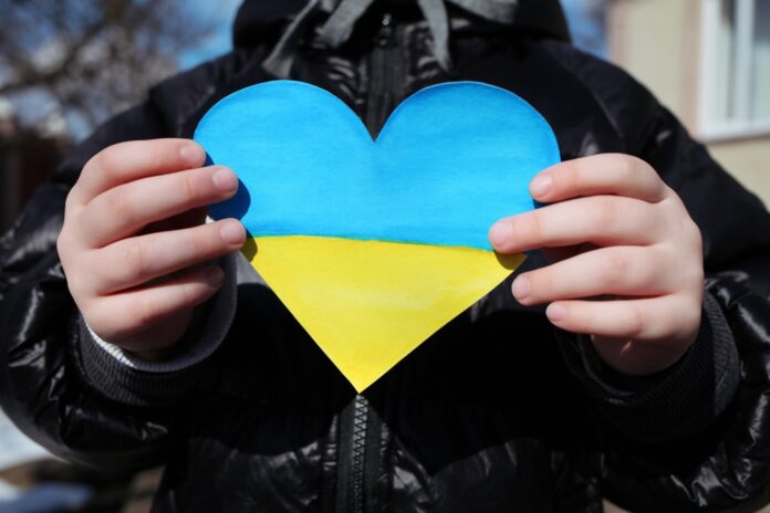 A small refugee boy from Ukraine with a drawing of the Ukrainian flag.