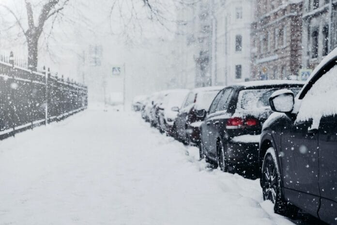 Beautiful city in snow. Cars covered with snow stand on parking place